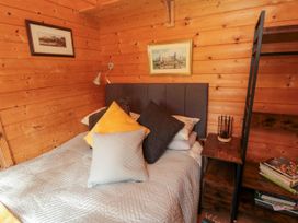 A bedroom with a bed with multiple pillows and wooden walls at Snape Castle Garden Lodge in Snape near Bedale