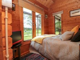 A bedroom with a bed pillows a blanket a small television and windows showing a garden at Snape Castle Garden Lodge Snape near Bedale