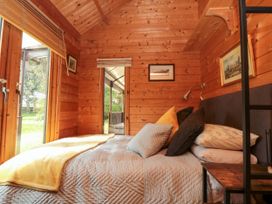 A bedroom with a bed pillows wall art a small table and wooden walls at Snape Castle Garden Lodge in Snape near Bedale