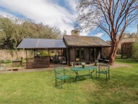 A garden with a green metal table and chairs in front of a small wooden building with a covered seating area at Snape Castle Garden Lodge in Snape near Bedale