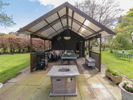 An outdoor covered seating area with a dining table, chairs, barbecue grill, fire pit, and garden furniture at Snape Castle Garden Lodge in Snape near Bedale