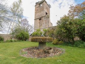 A garden with a stone fountain surrounded by grass and bushes with a stone tower in the background at Snape Castle Garden Lodge Snape near Bedale