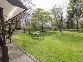 A garden with a metal table and chairs on the lawn surrounded by trees and a wooden fence at Snape Castle Garden Lodge in Snape near Bedale
