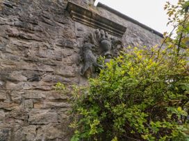 A stone wall with a carved coat of arms partially covered by green foliage at Snape Castle Garden Lodge in Snape near Bedale