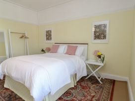 A bedroom with a bed with white bedding and striped pillows two framed pictures on the wall a white side table with a lamp and flowers and a wooden clothes rack with hangers at Rhos Retreat No 7 in Rhos-On-Sea