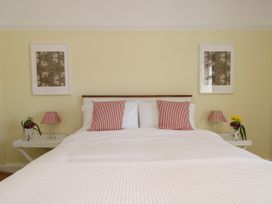 A bedroom with a double bed two red and white striped pillows two bedside tables with lamps and flowers and framed pictures on the wall at Rhos Retreat No 7 in Rhos On Sea