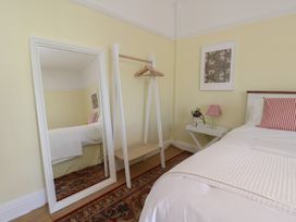 A bedroom with a bed a large mirror a small table with a lamp and flower and a clothes rack at Rhos Retreat No 7 in Rhos On Sea