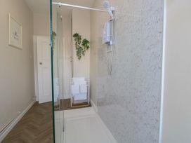 A shower area with a glass partition a showerhead on a marble wall white towels on a towel rack and a plant on the wall at Rhos Retreat No 7 in Rhos On Sea