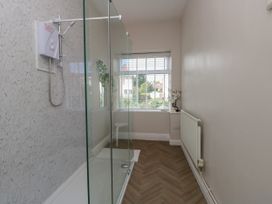 A bathroom with a walk-in shower, a window with blinds, a white stool, a radiator, and a small plant on the windowsill at Rhos Retreat No 7 in Rhos On Sea