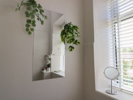 A corner of a room with a window with blinds a small round mirror on the window sill and a wall mirror with two hanging plants at Rhos Retreat No 7 in Rhos On Sea