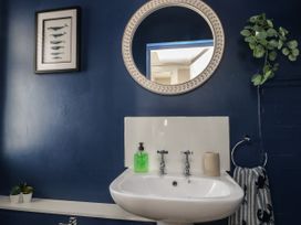 A bathroom sink with soap dispenser and towel under a round mirror and a fish picture on a dark blue wall at Rhos Retreat No 7 in Rhos On Sea