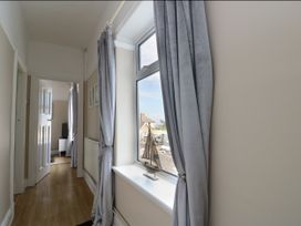 A hallway with light wood flooring a window with gray curtains and a model sailboat in the window at Rhos Retreat No Seven in Rhos On Sea
