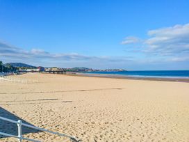 A sandy beach with railings on the left and buildings in the distance by the sea at Rhos Retreat No 7 in Rhos On Sea