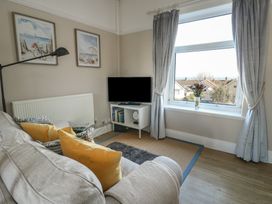 A living room with a sofa with yellow cushions a television on a stand a large window with curtains and two framed pictures on the wall at Rhos Retreat No 7 in Rhos-On-Sea