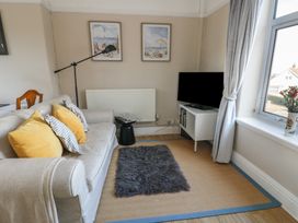 A living room with a grey sofa with yellow and striped pillows a TV on a stand a floor lamp and two paintings on the wall at Rhos Retreat No 7 in Rhos On Sea