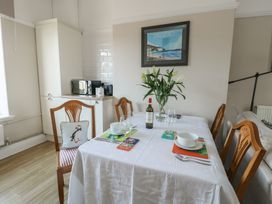 A dining table set with white tablecloth bowls wine glasses and a bottle of wine in a room with wooden chairs and a kitchen cabinet at Rhos Retreat No 7 in Rhos On Sea