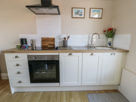A kitchen with white cabinets a built-in oven a stovetop a sink with a faucet cutting boards utensils mugs a kettle and flowers in a vase at Rhos Retreat No 7 in Rhos-On-Sea