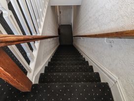 A staircase with dark patterned carpet and wooden handrails leading to a hallway at Rhos Retreat No 7 in Rhos On Sea