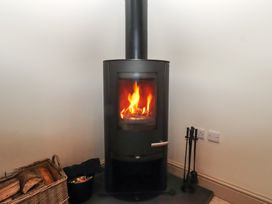 A wood stove with flames and a basket of logs at Cragg Lodge West Woodburn