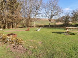 A garden with grass, wheelbarrow and trees at Cragg Lodge West Woodburn