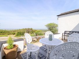 An outdoor patio with white metal table and chairs a planter with a small tree and a bench at Tan Y Merddyn in Ceunant near Llanrug