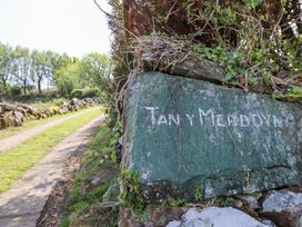 A dirt path lined with rocks and trees next to a green stone with the words Tan Y Merddyn near Llanrug