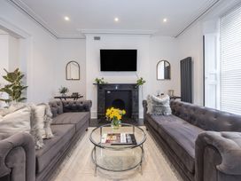 A living room with two gray sofas a round glass coffee table with flowers a black fireplace and a wall mounted TV at 8 Richmond Road in Exeter