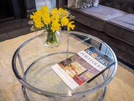 A glass coffee table with yellow flowers in a vase and magazines on a rug next to a dark sofa at 8 Richmond Road in Exeter
