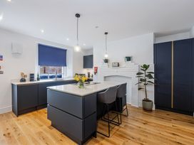 A kitchen with dark cabinets an island with chairs a window with a blue blind and wooden floor at 8 Richmond Road in Exeter
