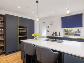 A kitchen with a white island countertop with two gray chairs and a flower vase and blue cabinets with built-in ovens and a window with a blue blind at 8 Richmond Road in Exeter