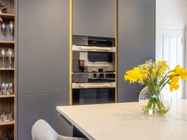 A kitchen with dark cabinets built in ovens glassware shelves and a vase with yellow flowers on a white countertop at 8 Richmond Road in Exeter
