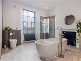 A bathroom with a freestanding bathtub a shower area a toilet a round mirror and a window at 8 Richmond Road in Exeter