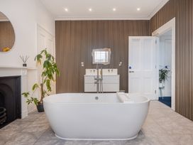 A bathroom with a freestanding bathtub a striped accent wall a plant a fireplace and a wall-mounted sink unit at 8 Richmond Road in Exeter