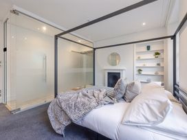 A bedroom with a canopy bed a glass-enclosed shower a fireplace a round mirror and built-in shelves with decor at 8 Richmond Road in Exeter