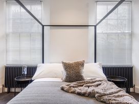 A bedroom with a bed and fur pillows between two windows at 8 Richmond Road in Exeter