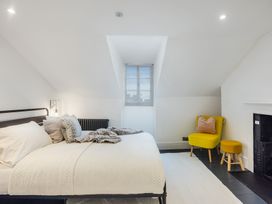 A bedroom with a bed pillows and blanket a yellow chair with a pillow a small stool and a fireplace at 8 Richmond Road in Exeter
