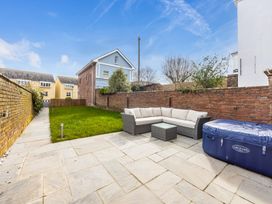 A patio area with a sectional sofa table and a hot tub next to a lawn and brick walls at 8 Richmond Road in Exeter