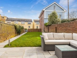 A backyard with a grass lawn a stone patio a wicker sofa with cushions and brick walls at 8 Richmond Road in Exeter