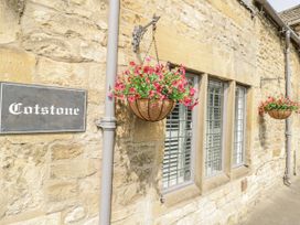 A stone wall with hanging flower baskets and a sign at Cotstone Cottage in Chipping Campden