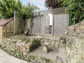 A garden with a stone wall and wooden gate at Cotstone Cottage Chipping Campden