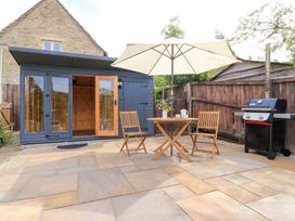 A patio with a table and chairs under an umbrella a barbecue and a wooden shed at Bramley Cottage near Cirencester