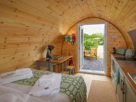 A wooden cabin interior with a bed, table with wine and glasses, kitchenette, and an open door leading outside at Moel Arthur in Bryniau Clwyd near Denbigh