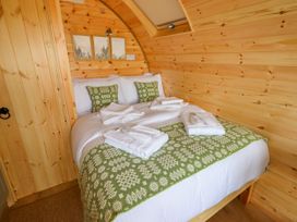 A bedroom with a bed covered in white bedding and green patterned pillows and blanket inside a wooden cabin at Moel Arthur in Bryniau Clwyd near Denbigh