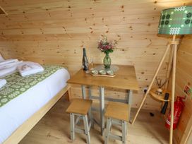 A wooden room with a bed, table with flowers, wine bottle, glasses, stools, and a floor lamp at Moel Arthur in Bryniau Clwyd near Denbigh