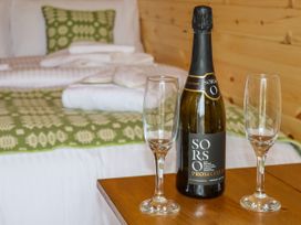 A bottle of prosecco and two empty glasses on a wooden table with a bed in the background at Moel Arthur in Bryniau Clwyd near Denbigh