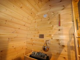A wooden sauna room with rocks on a heater a thermometer a water ladle and a caution sign at Moel Arthur in Bryniau Clwyd near Denbigh