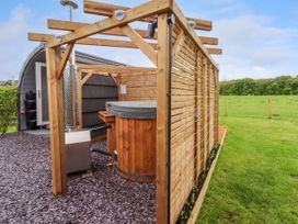 An outdoor wooden hot tub with privacy panels on a bed of slate chippings next to a small building in a grassy field at Moel Arthur in Bryniau Clwyd near Denbigh