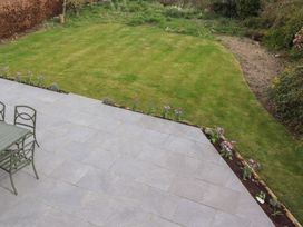 A backyard with a tiled patio featuring a green table and chairs next to a lawn with flower beds at Badachro in Lesbury