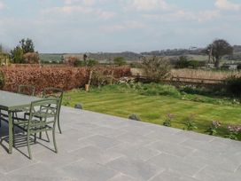 An outdoor patio with green chairs and table next to a lawn and hedge with fields and hills in the background at Badachro in Lesbury