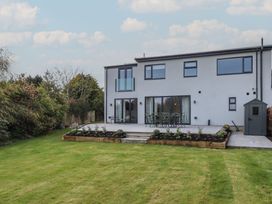 A backyard with a patio, garden shed, flower beds, grass lawn, and a modern two-story house at Badachro in Lesbury